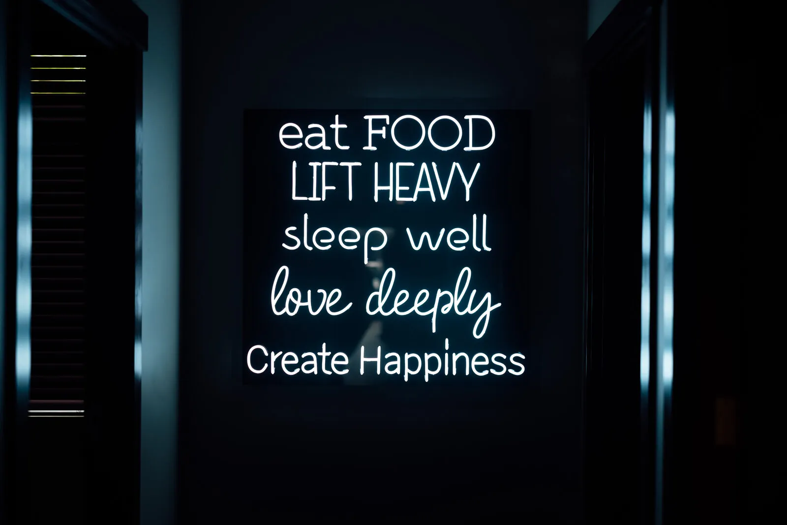 Neon sign at Asymmetric Health reading eat food, lift heavy, sleep well, love deeply, create happiness
