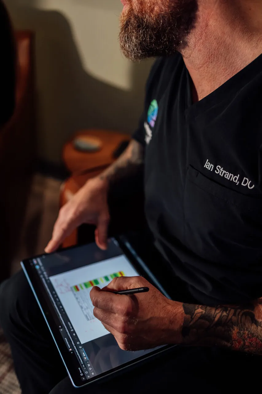 Close-up of Dr. Ian Strand marking up a patient's lab results on a tablet at Asymmetric Health, showing color-coded biomarker ranges