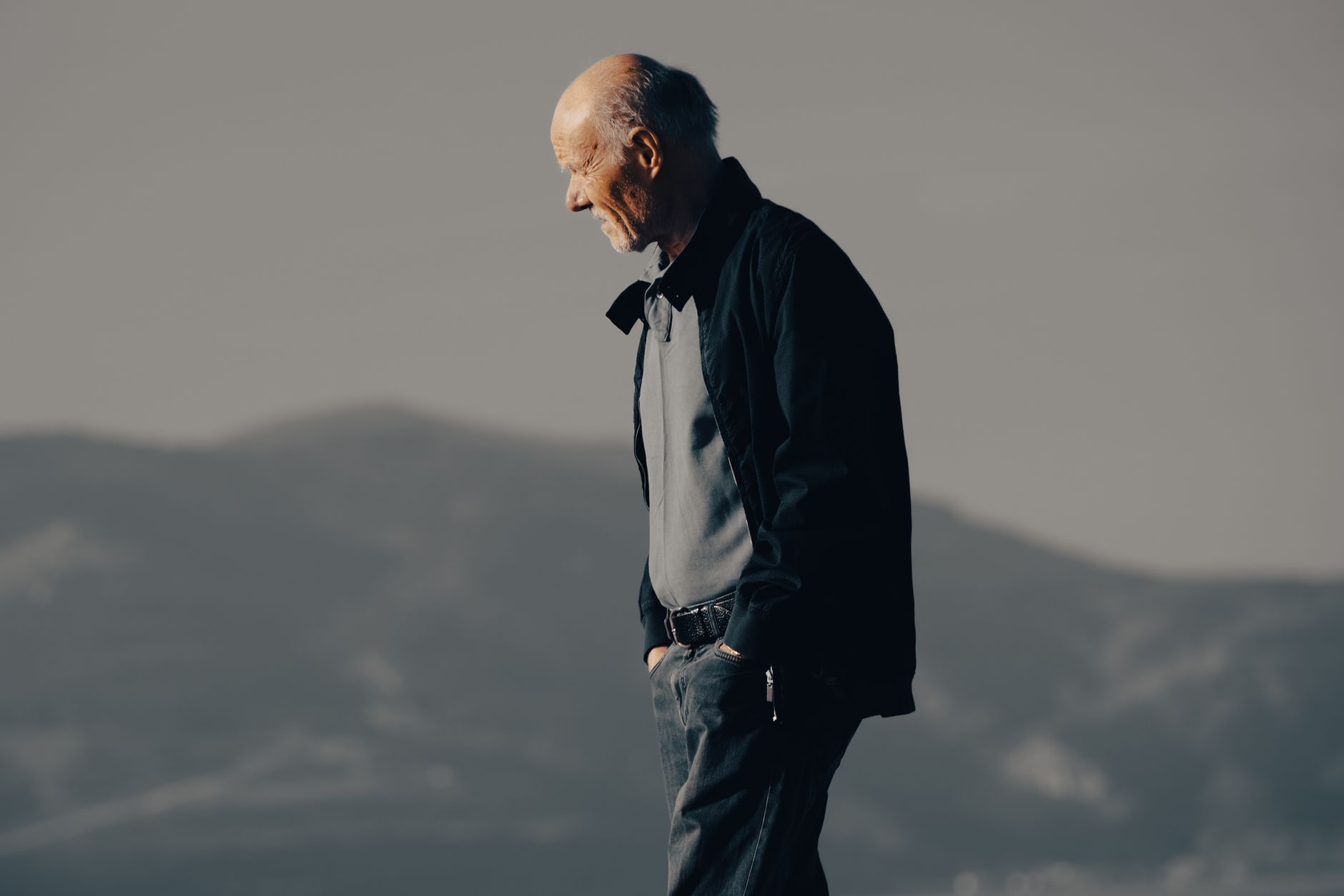 Older man walking outdoors with his hands in his pockets against a mountain backdrop, illustrating an educational article on age-related testosterone decline in men