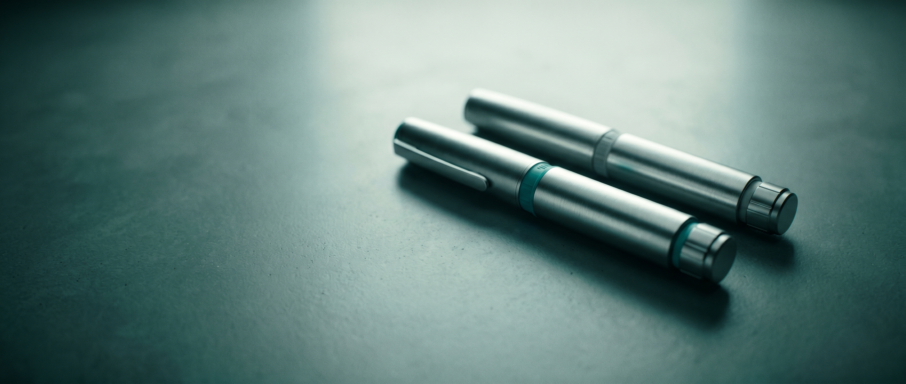 Two GLP-1 injection pens side-by-side on a dark surface, illustrating a clinical comparison of retatrutide and tirzepatide weight loss medications