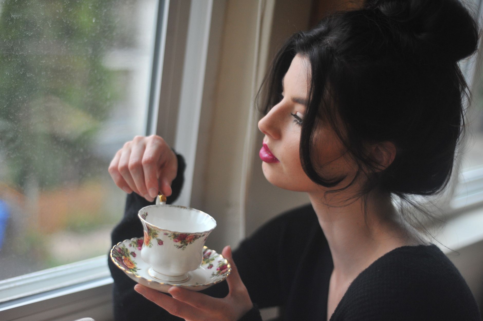 Woman sitting beside a window stirring a cup of tea in a quiet moment at home, illustrating an educational article on the signs of low estrogen