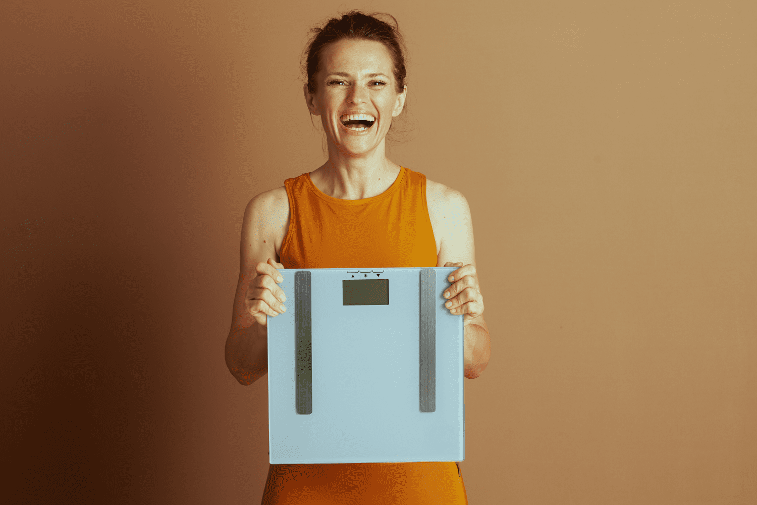 weight loss a woman in yellow shirt smiling an holding a scale
